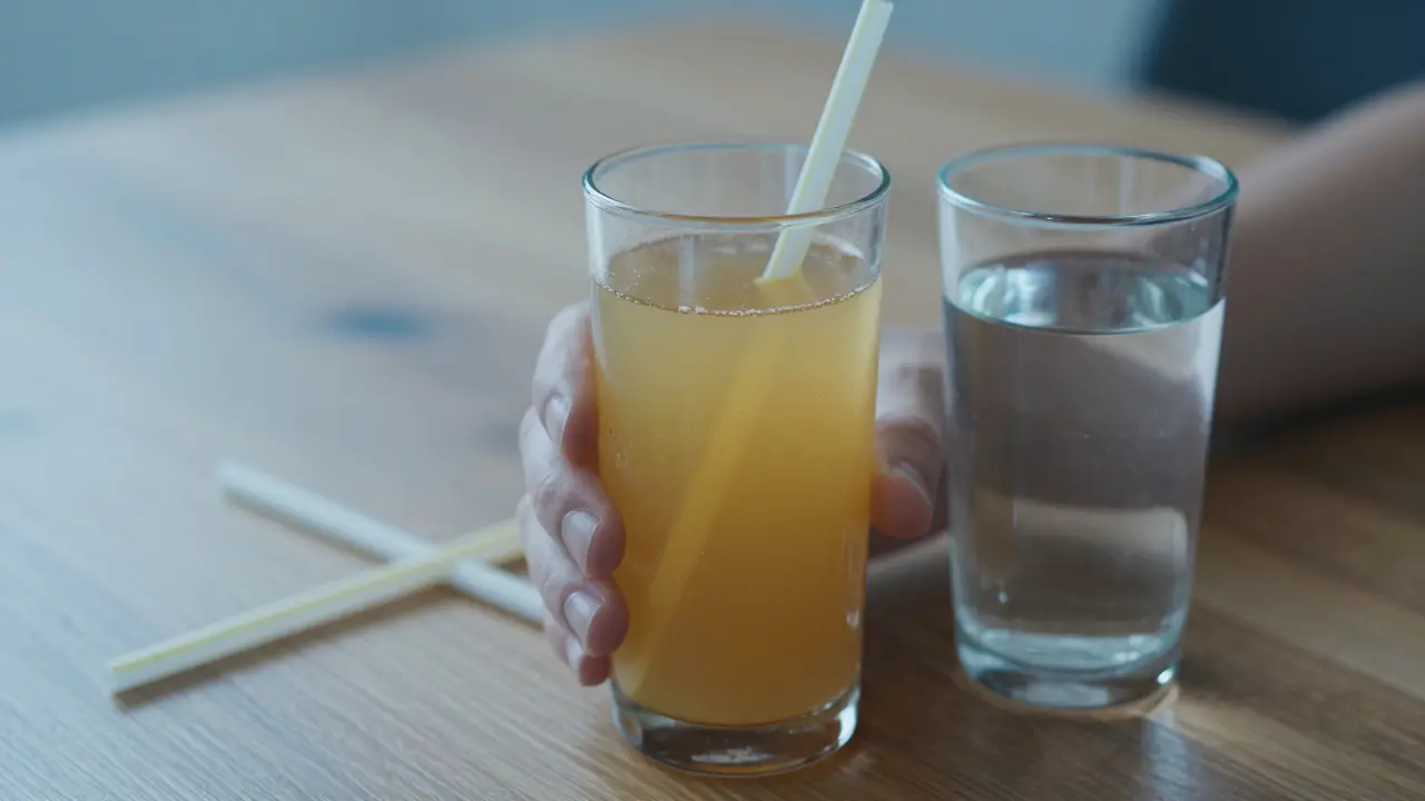 Sklenice vody a jablečného džusu bez brčítka na dřevěném stole.